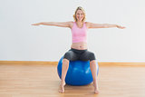 Smiling blonde pregnant woman sitting on exercise ball