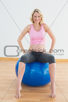 Happy blonde pregnant woman sitting on exercise ball