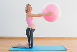 Happy blonde pregnant woman lifting exercise ball