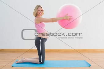 Happy blonde pregnant woman lifting exercise ball