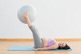 Smiling pregnant woman lifting exercise ball with legs
