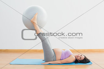 Smiling pregnant woman lifting exercise ball with legs
