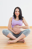 Pregnant woman sitting on floor holding belly smiling at camera