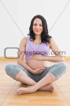 Pregnant woman sitting on floor holding belly smiling at camera