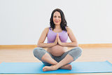 Pregnant woman sitting on mat in lotus pose smiling at camera