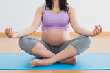 Pregnant brunette sitting on mat in lotus pose