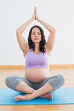 Pregnant brunette sitting on mat in lotus pose meditating