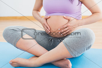 Pregnant woman sitting on mat in touching her belly