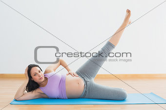 Smiling pregnant woman lying on mat lifting her leg