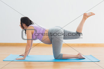 Pregnant brunette kneeling on mat doing pilates