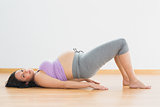 Pregnant brunette lying on floor in bridge pose