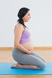 Happy pregnant brunette kneeling on exercise mat