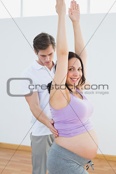 Happy pregnant woman doing yoga with a personal trainer