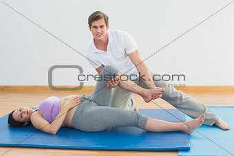 Masseur moving pregnant womans leg on blue mat smiling at camera