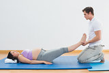 Masseur lifting pregnant womans legs on blue mat
