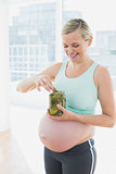 Blonde pregnant woman eating from jar of pickles