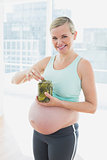 Smiling blonde pregnant woman eating from jar of pickles
