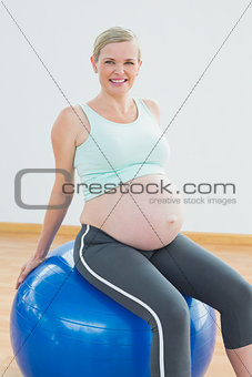 Happy blonde pregnant woman sitting on blue exercise ball