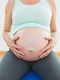Pregnant woman sitting on blue exercise ball holding her belly