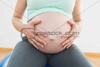 Pregnant woman sitting on exercise ball holding her belly
