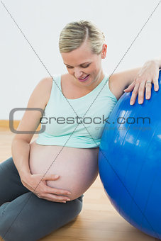 Smiling pregnant woman leaning against exercise ball holding her belly
