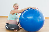 Smiling pregnant woman sitting beside exercise ball