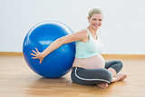 Happy pregnant woman sitting beside exercise ball