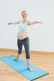 Blonde pregnant woman doing yoga on blue mat smiling at camera