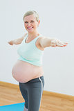 Blonde pregnant woman doing yoga on mat smiling at camera