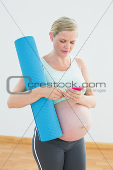 Pregnant woman holding exercise mat sending a text message