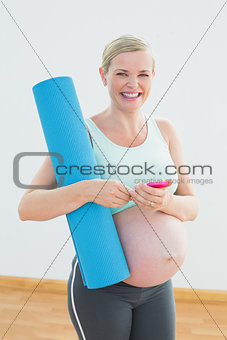 Happy pregnant woman holding exercise mat sending a text message