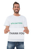 Smiling young male volunteer holding 'thank you' paper