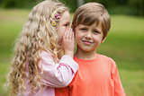 Girl whispering secret into boy's ear at park
