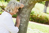 Thoughtful senior woman leaning to tree at park