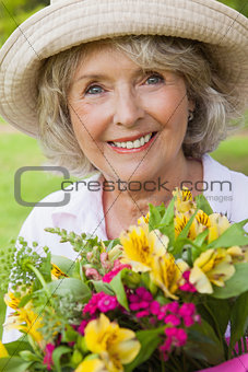 Close-up of a smiling mature woman holding flowers at park