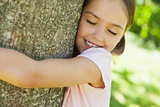 Smiling girl hugging tree with eyes closed at park
