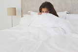 Girl hiding face behind sheet in bed