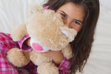 Smiling girl with stuffed toy sitting on bed