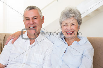 Retired couple sitting on couch smiling at camera