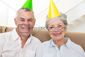 Senior couple sitting on couch wearing party hats