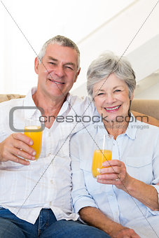 Senior couple sitting on couch drinking orange juice