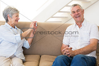 Retired woman taking photo of her partner on the couch