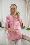 Pregnant woman holding apple in kitchen