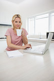 Woman using laptop while drinking coffee in kitchen