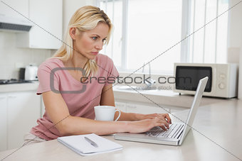 Side view of a serious woman using laptop in kitchen