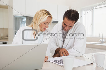 Casual business couple with laptop looking at graphs in kitchen
