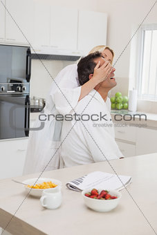 Woman covering man's eyes at breakfast table in kitchen