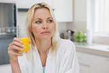 Thoughtful woman with orange juice in kitchen