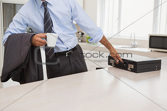 Well dressed man with coffee cup picking briefcase in kitchen