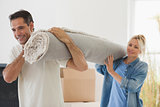 Couple carrying rolled rug after moving in a house